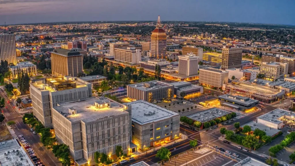 Aerial view of downtown Fresno County, CA, at dusk showcasing city buildings, streets, and skyline illuminated by vibrant evening lights.