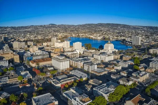 Aerial view of downtown Oakland, California featuring Lake Merritt, the Alameda County Courthouse, and surrounding city buildings under a clear blue sky.