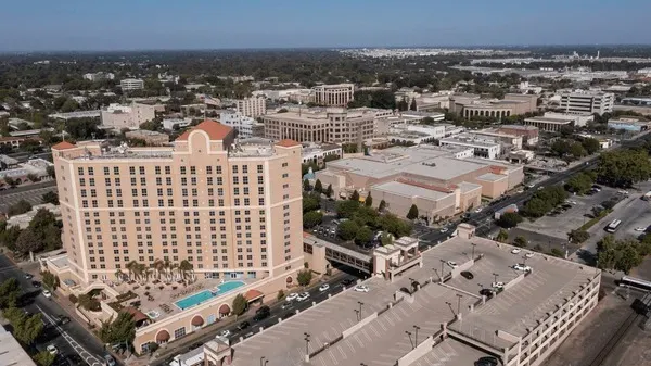 Aerial view of downtown Modesto, CA with tall hotel building, pool, parking structure, and cityscape in the background.
