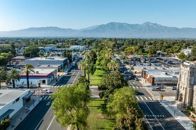 Aerial view of downtown Ontario, CA, featuring palm-lined streets, commercial buildings, and a scenic backdrop of the San Gabriel Mountains on a clear day.