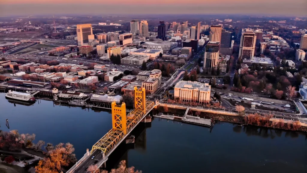 Aerial view of downtown Sacramento County, California, featuring the Tower Bridge spanning the Sacramento River at sunset.