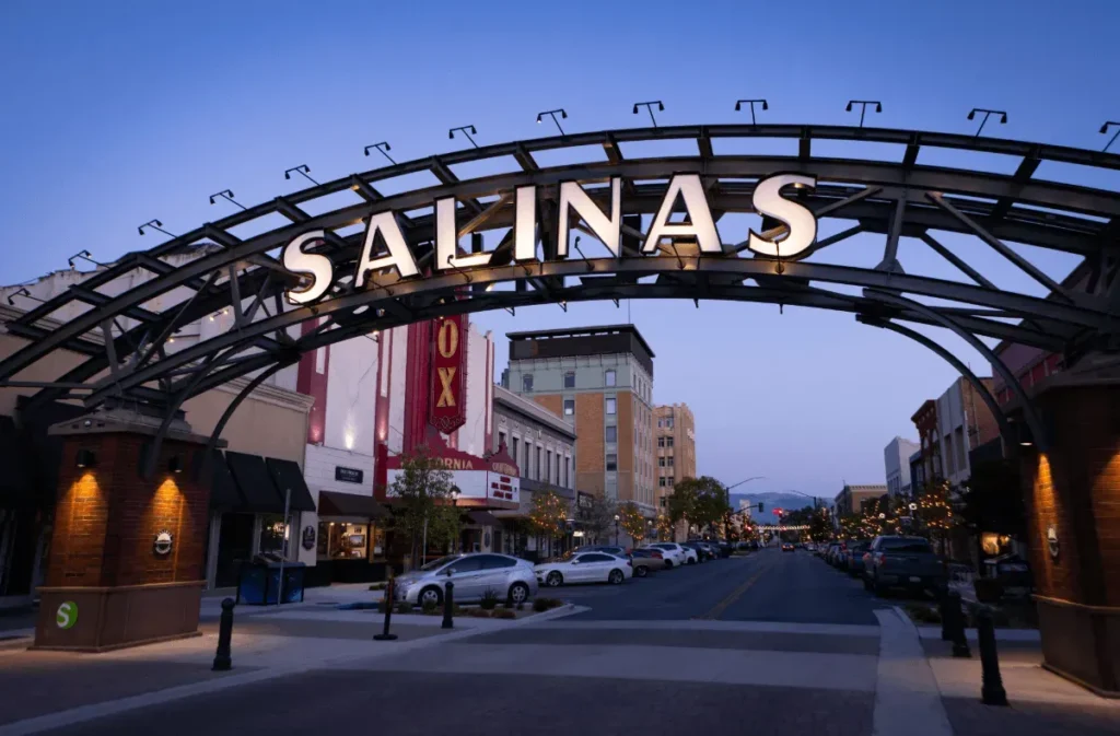 Downtown Salinas, CA at dusk featuring the illuminated Salinas archway and historic buildings along Main Street.