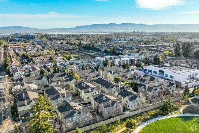 Aerial view of a residential neighborhood in Sunnyvale, California, with rows of homes, green spaces, and mountains in the background under a bright blue sky.