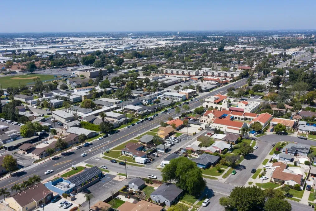 Aerial view of a suburban neighborhood and commercial area in Fullerton, CA, showing streets, buildings, homes, and surrounding city landscape on a clear day.