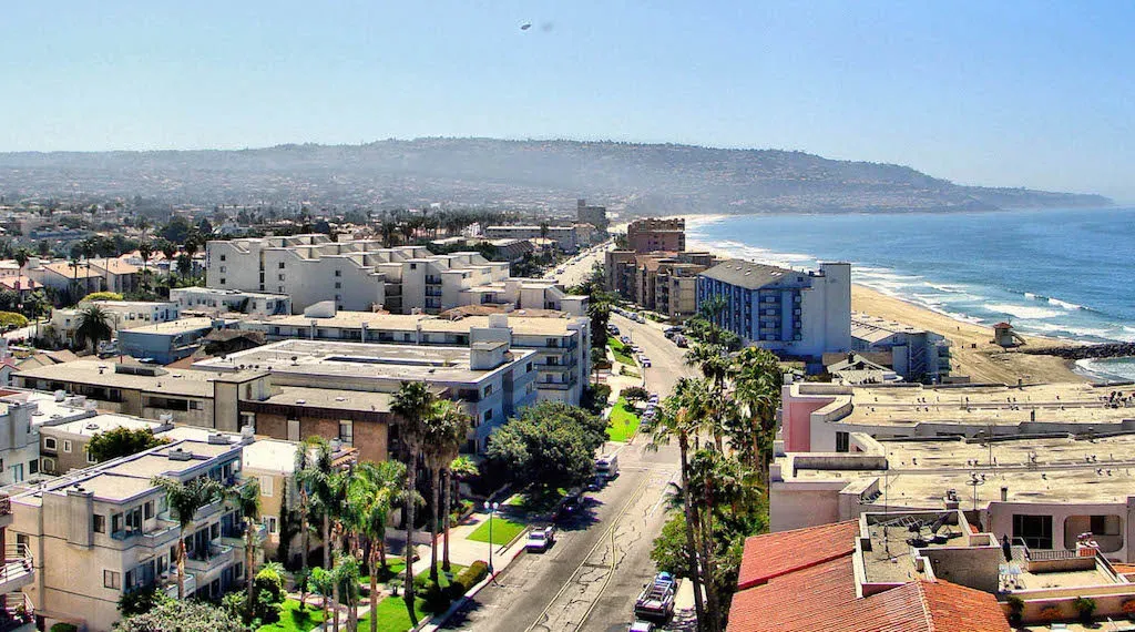 Aerial view of coastal buildings and beachside neighborhoods in Torrance, CA, showing the shoreline, ocean, and residential area on a sunny day.