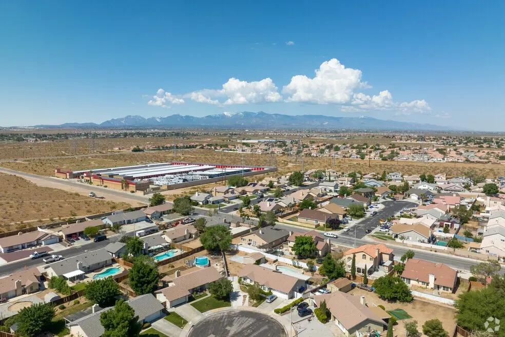 Aerial view of residential neighborhoods in Victorville, CA, with desert landscape, distant mountains, and clear blue skies in the background.