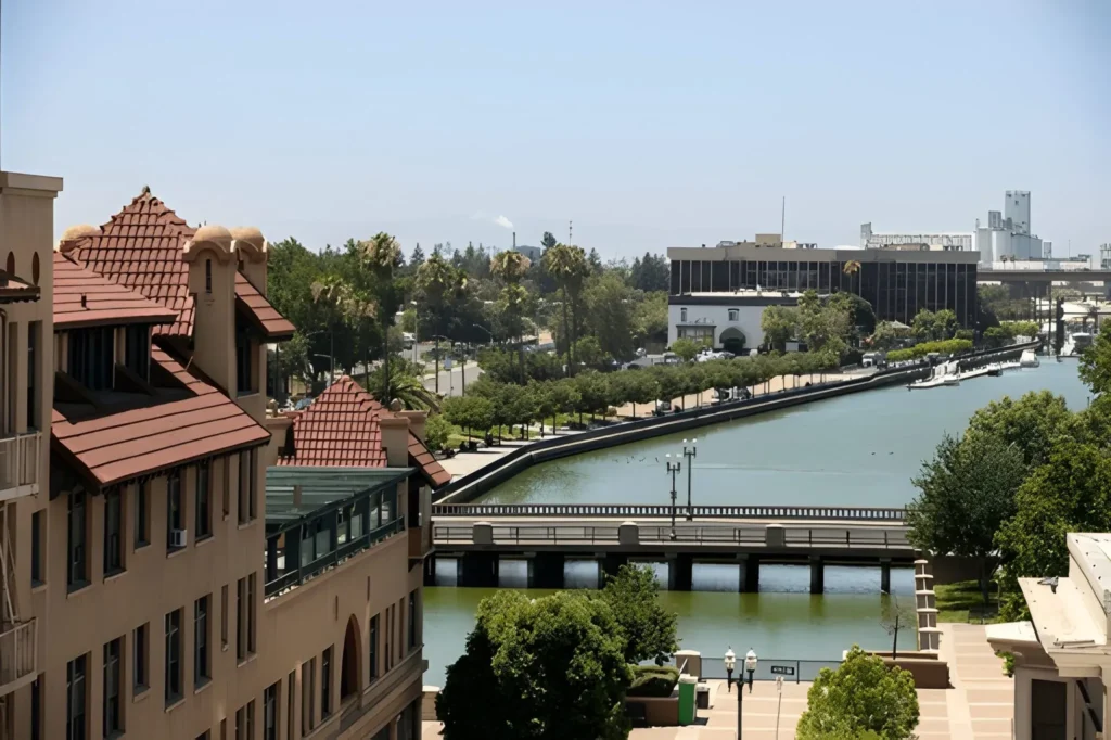 scenic view of downtown Stockton in San Joaquin County, California, featuring the waterfront canal, bridges, and surrounding buildings under a clear blue sky.