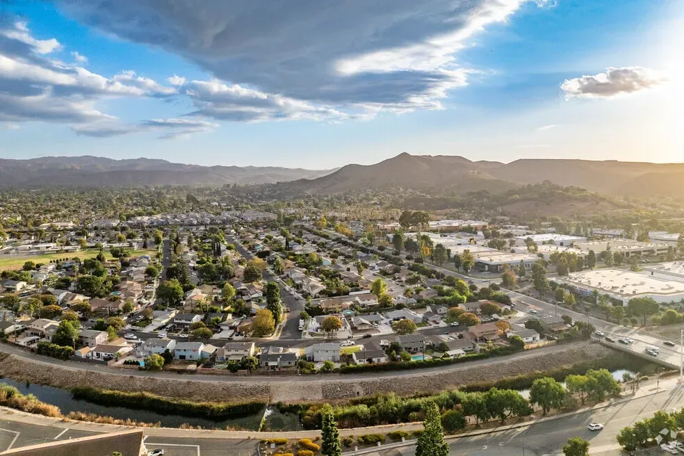 Aerial view of Simi Valley, CA, featuring residential neighborhoods, roads, and surrounding hills under a bright sunset sky.