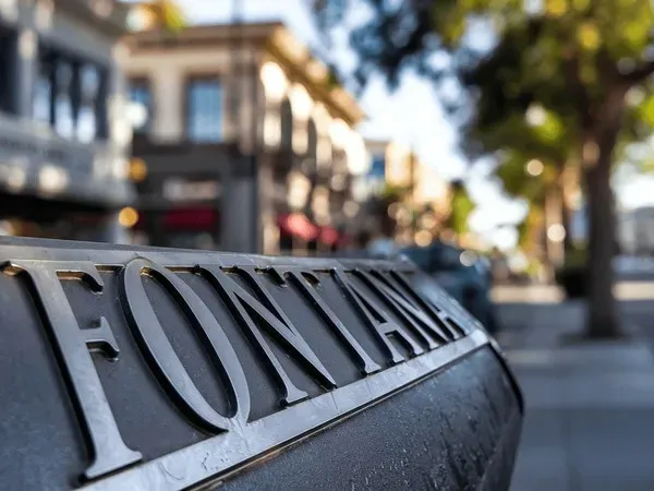 Close-up of a Fontana city sign with blurred downtown shops and trees in the background, Fontana, CA.