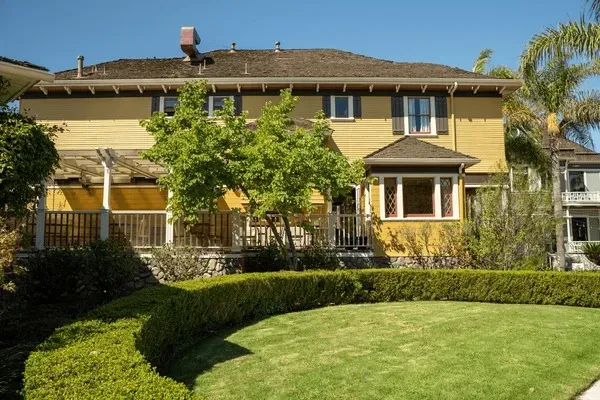 Historic yellow house with manicured lawn, hedges, and palm trees in Oxnard, CA.