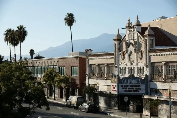 Historic California Theatre and palm-lined street in downtown San Bernardino, CA with mountain backdrop.