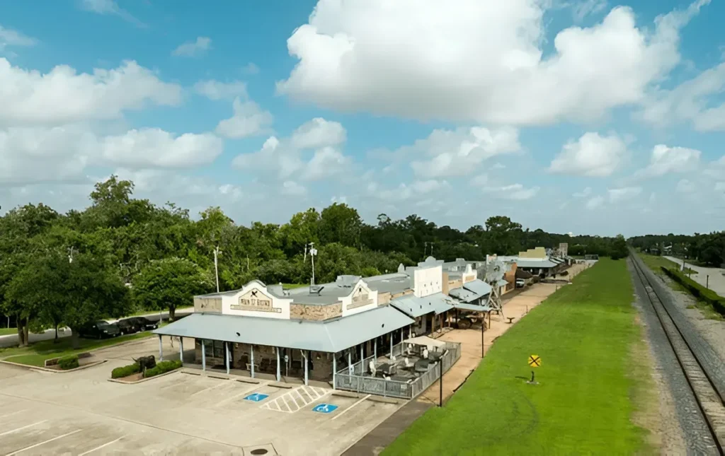 Historic storefronts and railway line in League City, Texas, showcasing old-town charm and green spaces.
