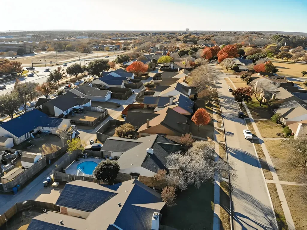 Aerial view of a residential neighborhood in Flower Mound, Texas, showcasing suburban homes, autumn trees, and nearby roads under a clear blue sky.