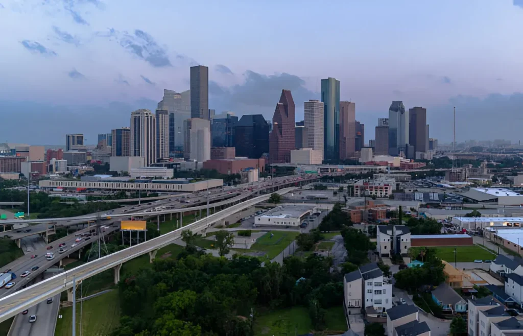 Aerial view of Katy, Texas at dusk, showcasing the Houston skyline, major highways, residential neighborhoods, and modern high-rise buildings.