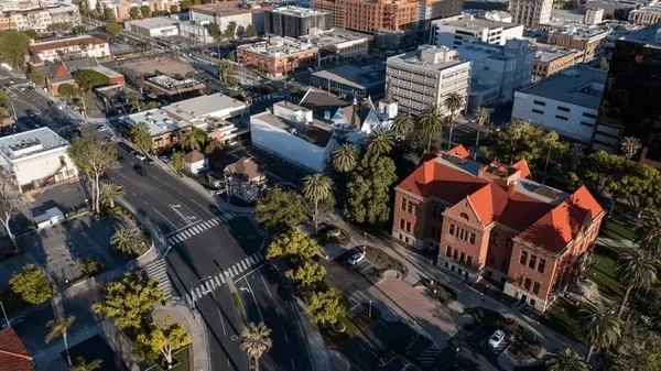 Aerial view of a city intersection featuring palm trees, historical buildings, and modern architecture amidst bustling streets.